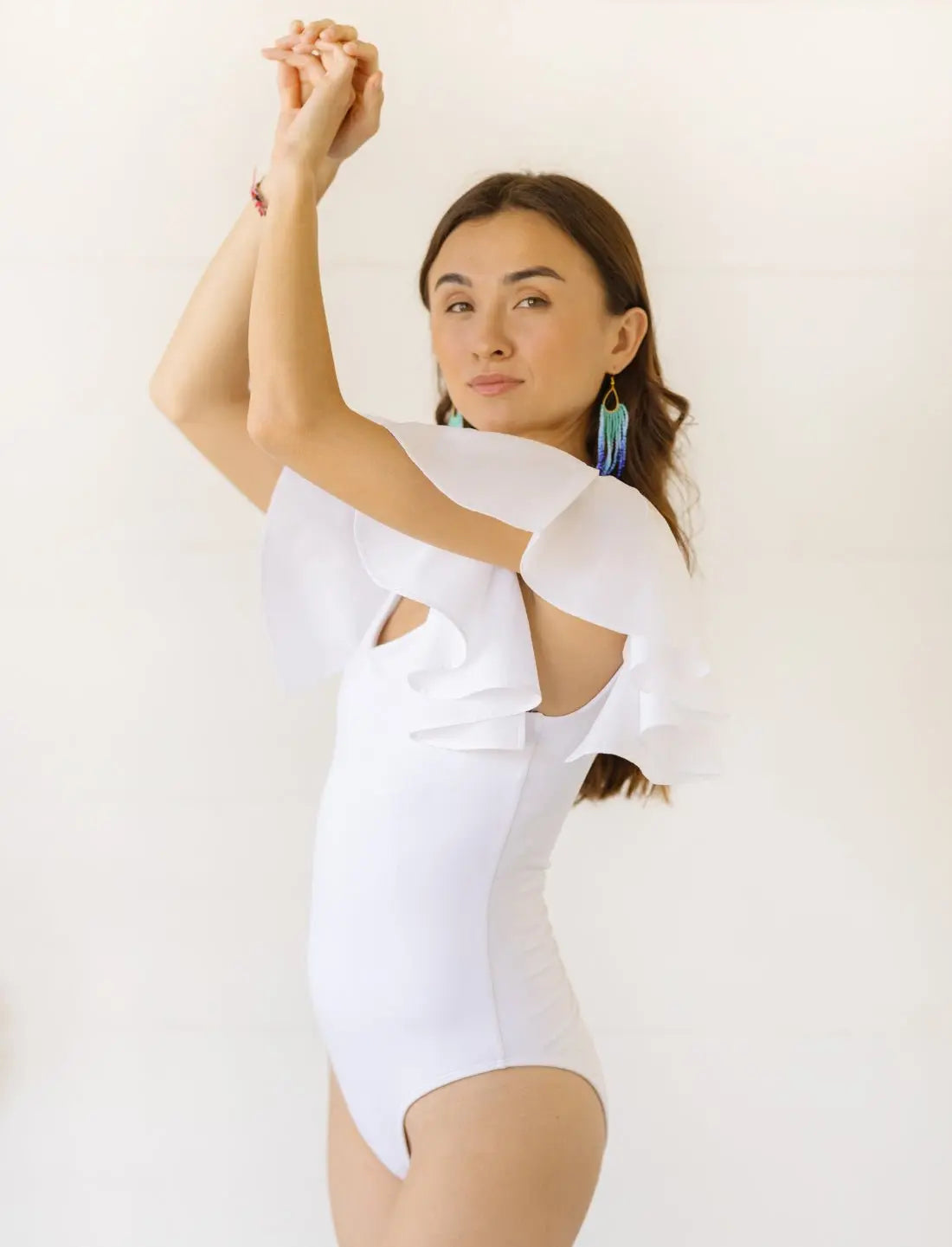 A model posing with her arms raised, wearing the white Ina Bodysuit with flutter sleeves. The image highlights the bodysuit's form-fitting silhouette