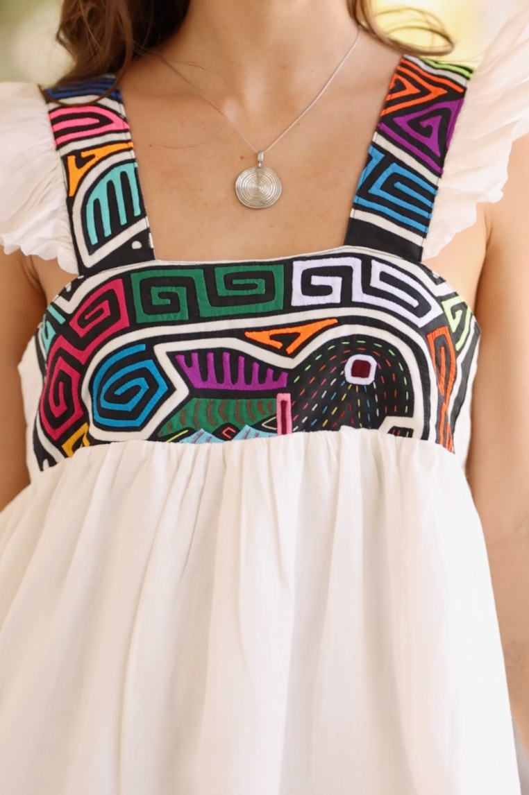 Video showcases the Yemaya Embroidery Adult Gown as the model twirls and walks. The gown moves elegantly, giving the model a feminine and graceful aesthetic. The colorful mola embroidery is eye-catching and beautiful against the soft white linen of the dress. 