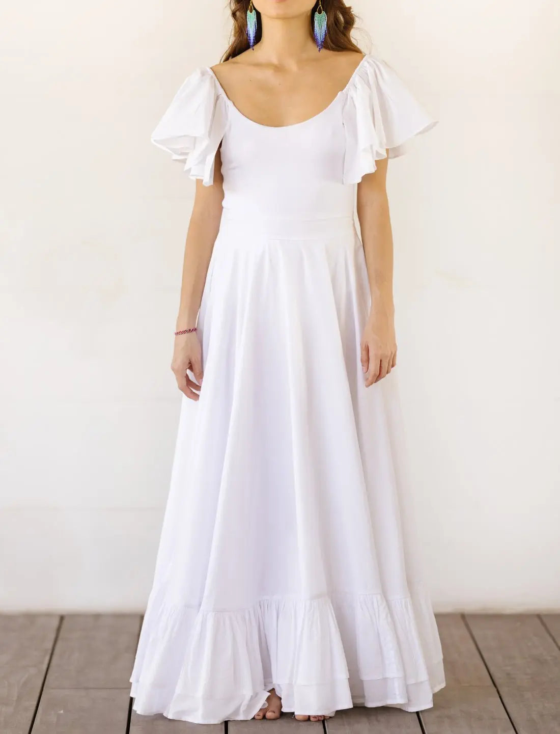 Sacred Hoop of Life Maxi Skirt in crisp white with matching flutter sleeve Ina Bodysuit top and colorful beaded statement earrings. Bohemian wedding dress, ethical fashion, sustainable clothing, beach ceremony gown, simple bridal dress, ruffle hem design, handcrafted apparel, minimalist wedding style, artisan made clothing, summer bridal attire, barefoot elegance photographed against clean white background.