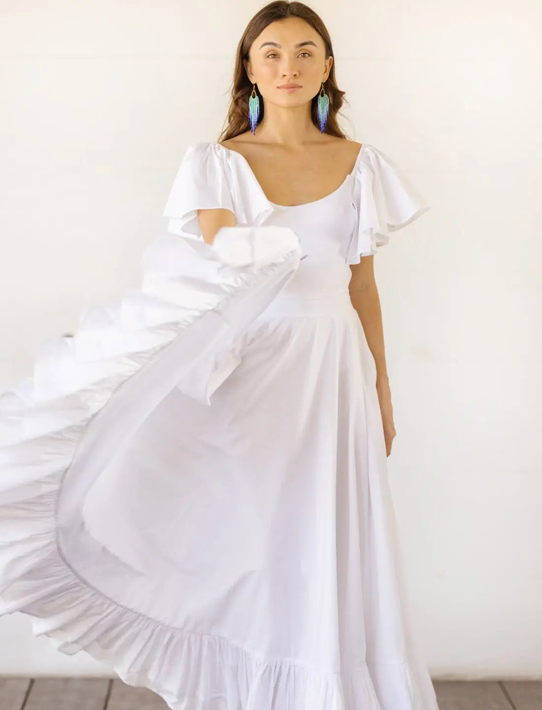 Sacred Hoop of Life Maxi Skirt in pure white with flowing movement, paired with matching flutter sleeve bodysuit top and vibrant beaded earrings. Bohemian wedding dress, ethical fashion, sustainable clothing, beach ceremony gown, simple bridal dress, ruffle hem detail, lightweight fabric motion, handcrafted apparel, minimalist wedding style, artisan made clothing, summer bridal attire photographed against clean white background.