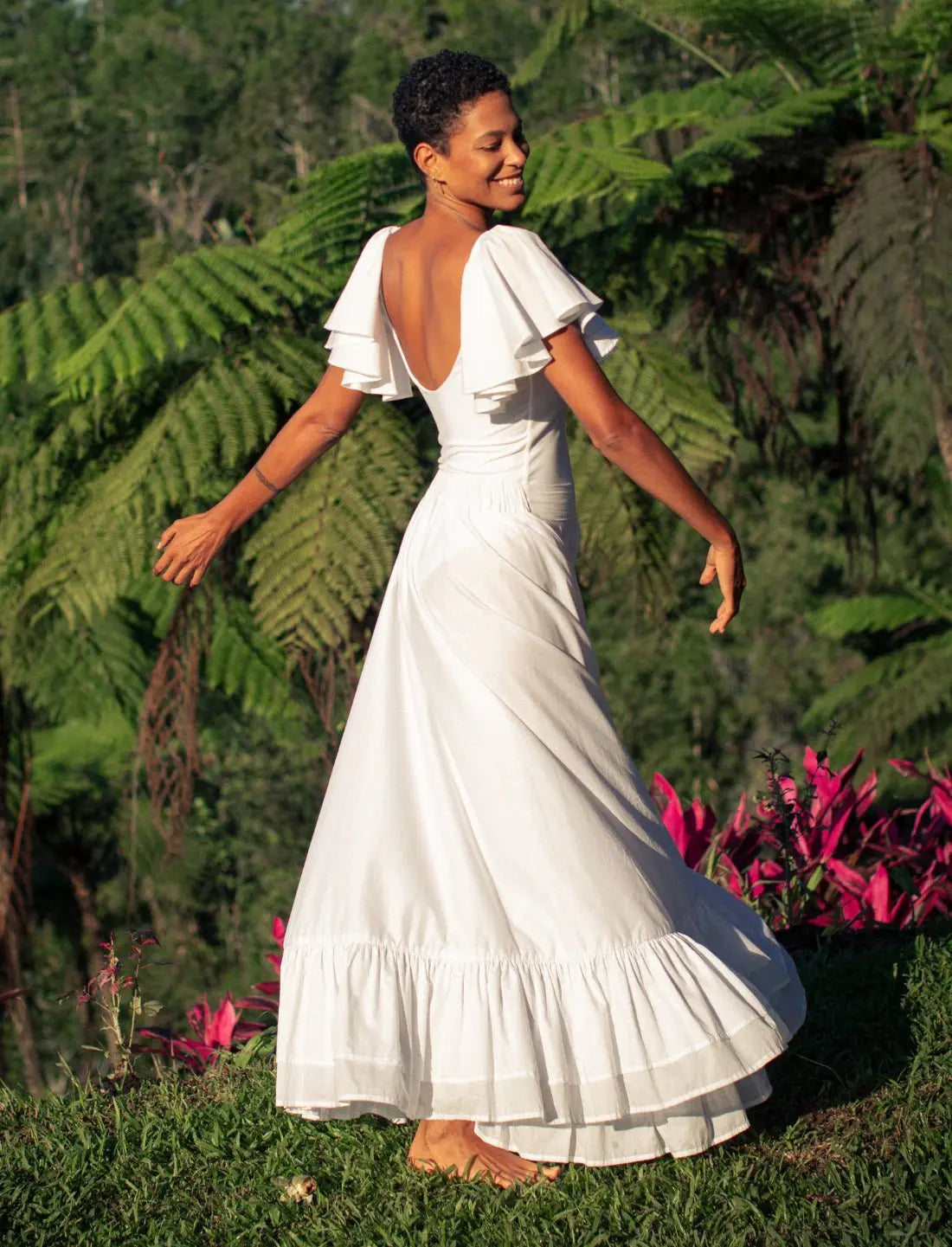 Sacred Hoop of Life Maxi Skirt in ivory white with matching flutter sleeve top, showcasing elegant open back design. Bohemian wedding dress, ethical bridal fashion, sustainable clothing, beach ceremony gown, destination wedding attire, ruffle hem detail, handcrafted apparel, summer wedding dress, artisan made clothing, barefoot bride, natural wedding gown photographed against lush tropical fern backdrop.
