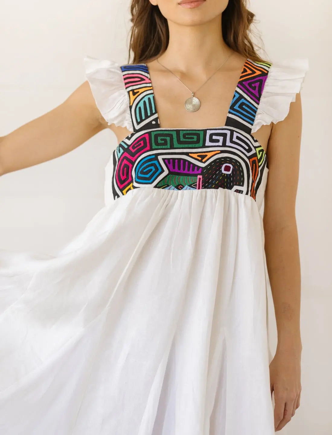 A close-up image of the mola pattern featured on the Yemaya Embroidery Adult Gown. It has colorful geometric patterns and shapes including a fish. 