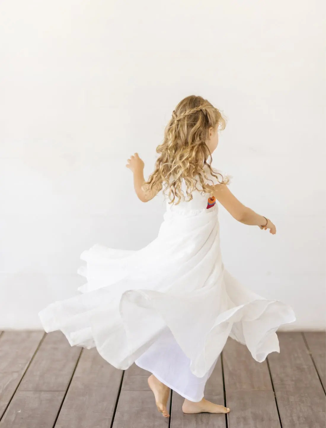 A young blonde girl twirls away from the camera, her Yemaya Embroidery Child Gown twisting and flowing as she moves with total comfort and ease.