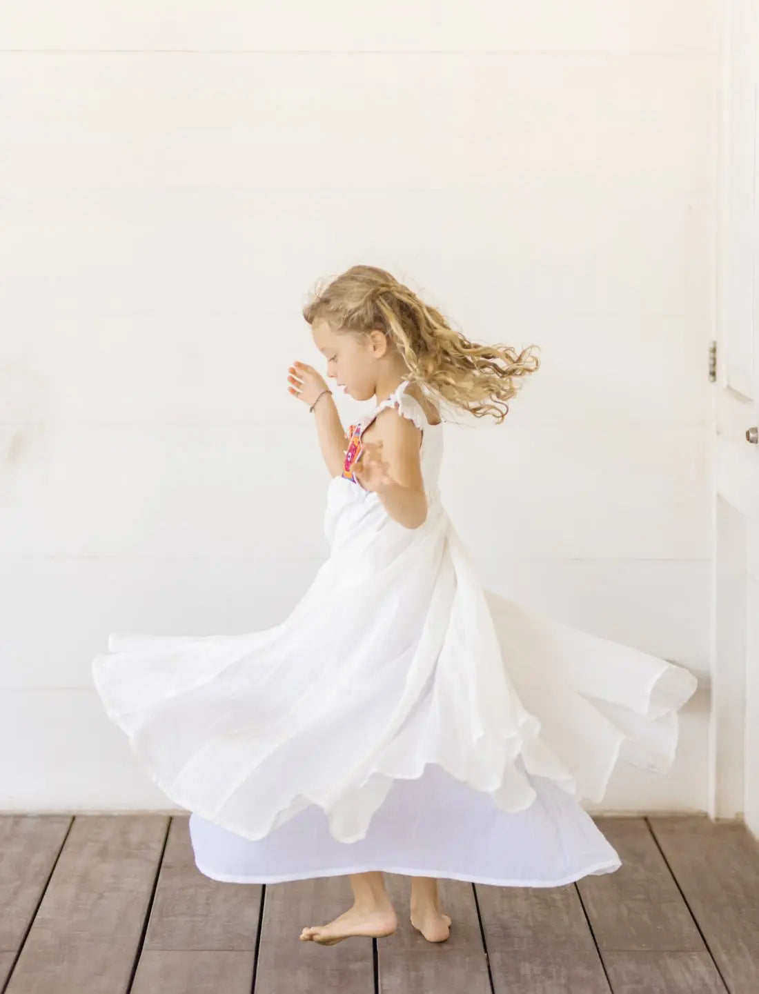 A young girl is captured mid-twirl in the Yemaya Embroidery Child Gown, the skirt flowing outward in a perfect carousel. It's a darling moment, as the young girl moves in delight as the dress envelops her in child-like wonder and beauty.